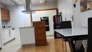 A modern kitchen with white cabinets, a wooden island, a black chair, and a painting on the wall. - Amber Hostel Szlak (Kraków)
