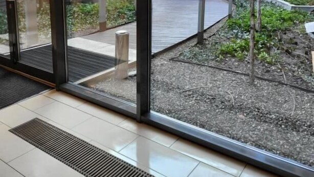 A modern building with large glass doors, a tiled floor, and a view of a courtyard with plants and a pathway. - Amber Hostel Szlak (Kraków)