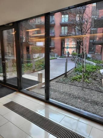 A modern building with large glass doors, a tiled floor, and a view of a courtyard with plants and a pathway.