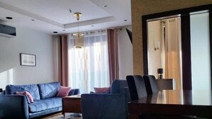 A modern living room with a sofa, a dining table with chairs, and a large window with curtains. - Amber Hostel Szlak (Kraków)