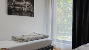 A bedroom with a bed, a bench, and a large window with sheer curtains. - Amber Hostel Szlak (Kraków)