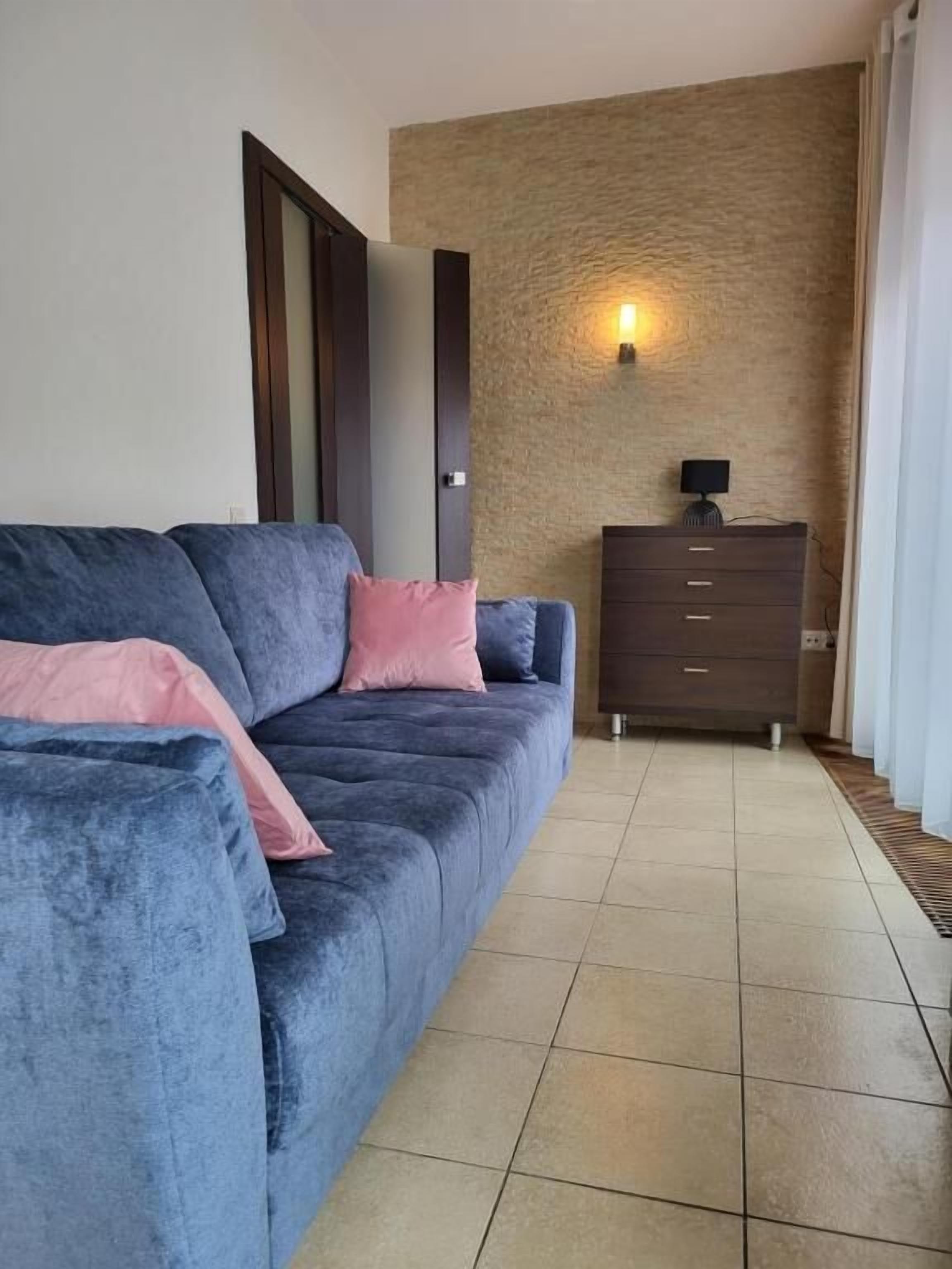 Un salón con un sofá azul oscuro, un aparador de madera y una pared con textura.