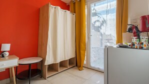 A room with a red wall, a white desk with a lamp, a wooden cabinet, a shower curtain, and a glass door with yellow curtains. - Studio Apartment 'La Dolce Vita 2' with Shared Pool, Private Terrace and Air Conditioning (Lambesc)