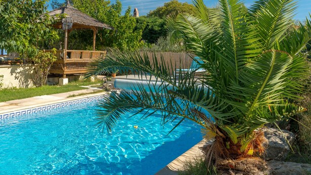 A swimming pool with a thatched gazebo, surrounded by lush greenery and a clear blue sky. - Studio Apartment 'La Dolce Vita 2' with Shared Pool, Private Terrace and Air Conditioning (Lambesc)