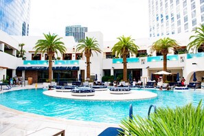 A hotel pool area with multiple levels, palm trees, and lounge chairs.