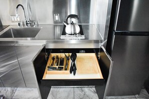 A stainless steel kitchen with a drawer organizer containing utensils and a cutting board.