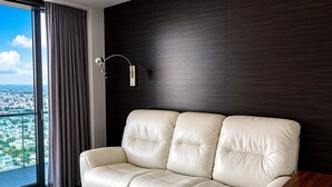 A modern living room with a leather sofa, a wooden side table, and a view of a cityscape through a large window.
