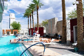 Un espace piscine avec des chaises longues, des palmiers et un bâtiment portant l’inscription « PALMS ».