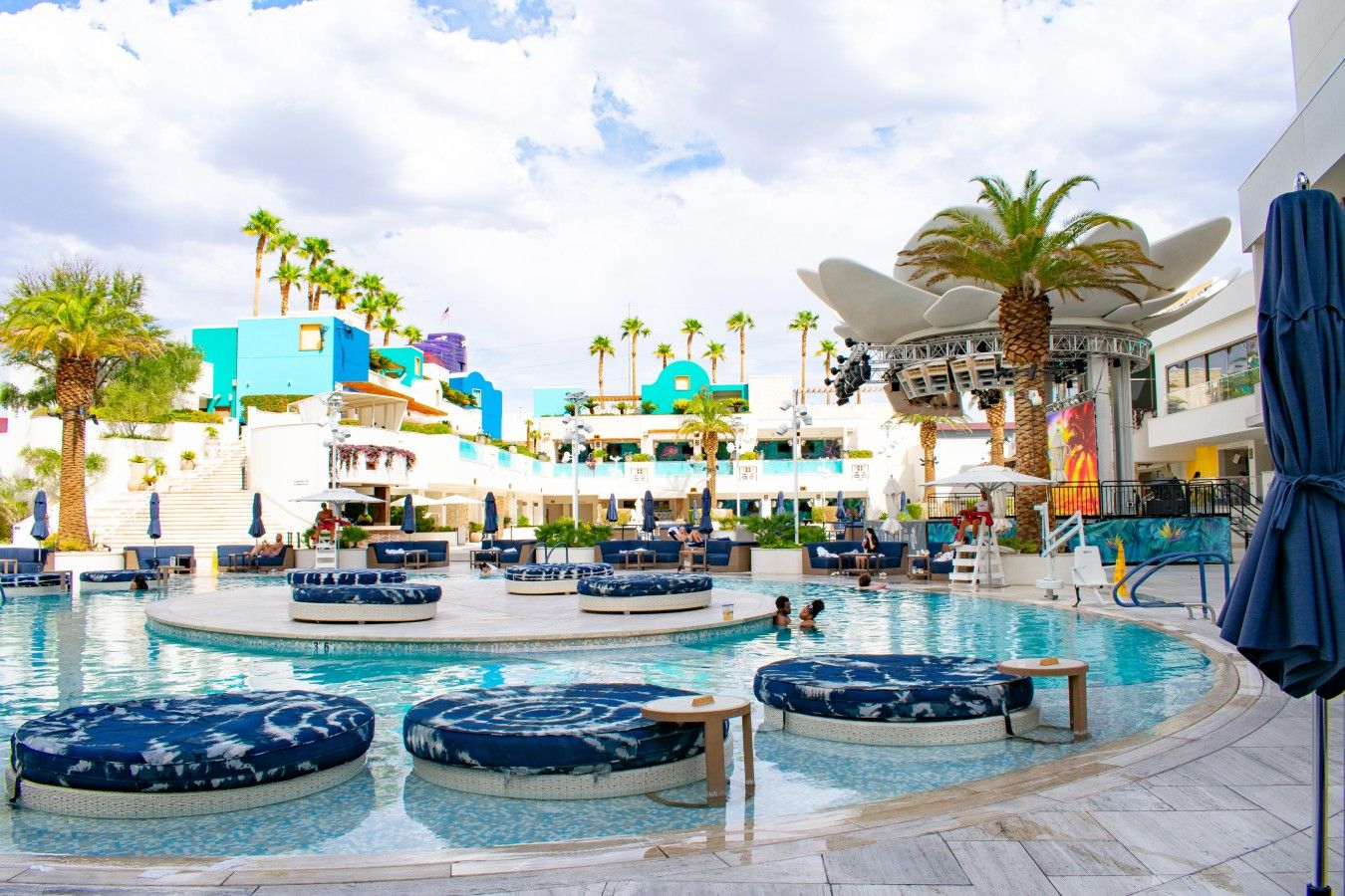 A hotel pool area with multiple levels, palm trees, and outdoor seating.