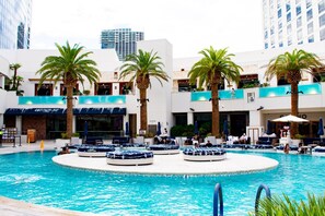 Un espace piscine d’hôtel avec de nombreux chaises longues et des palmiers.