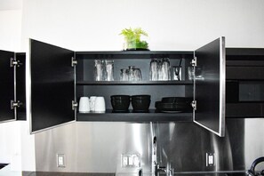 A kitchen with open cabinets displaying glassware, bowls, and a potted plant.