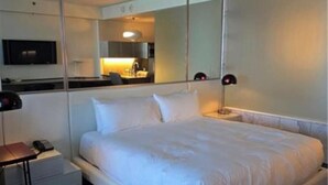 A modern hotel room with a large bed, a bedside table with a lamp, a TV mounted on the wall, and a mirror reflecting the room.