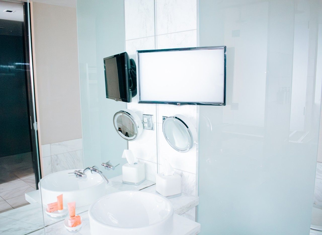 A modern bathroom with a large mirror, two sinks, and a glass-enclosed bathtub.