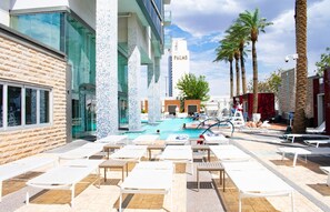 Un espace piscine avec des chaises longues, une piscine et des palmiers.