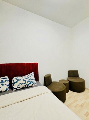 A bedroom with a bed, two pillows, a red headboard, and three round chairs.