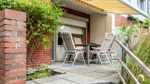 Une terrasse avec une table et des chaises, un mur en briques et un espace abrité surmonté d’une marquise à rayures.