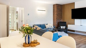 Un salon moderne avec un canapé, une table à manger agrémentée d’un vase de fleurs, un téléviseur fixé au mur et un mur décoratif en briques.