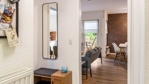 Un couloir mène à une salle à manger où l’on trouve un mur en briques, un miroir et une petite table sur laquelle est posé un livre.