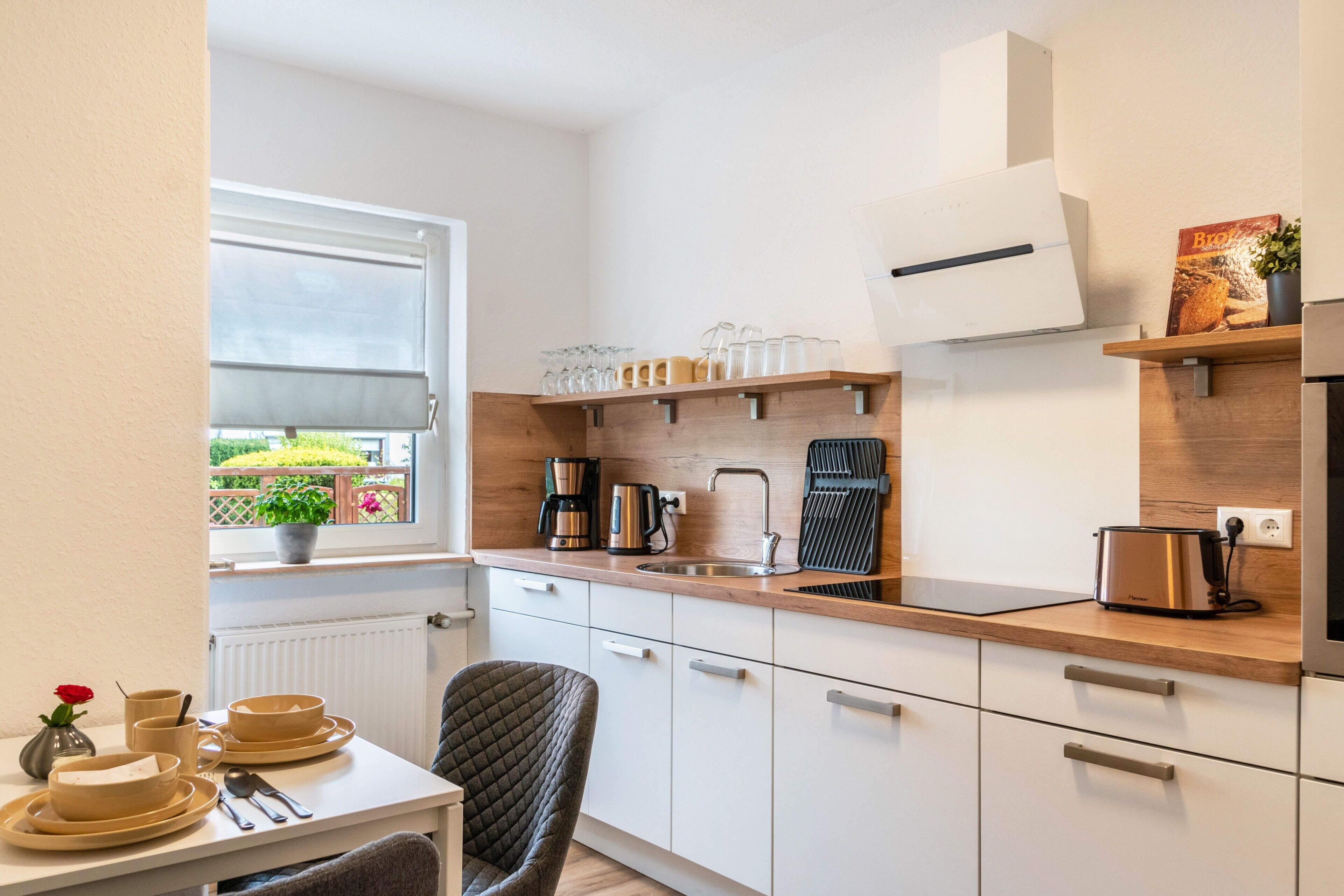 A compact kitchen with a window, a dining table with plates and cutlery, and a chair.