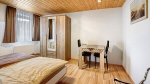 A bedroom with a wooden ceiling, a bed, a desk with two chairs, a radiator, and a window with curtains. - Apartment 'Ferienwohnung Annette' with Shared Terrace and Wi-Fi (Gomadingen)