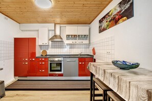 Een keuken met rode en witte kastjes, een roestvrijstalen afzuigkap en een houten plafond.