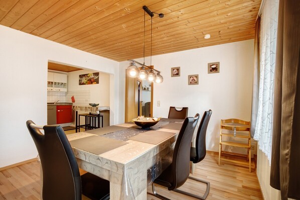 Un comedor con techo de madera, una mesa con sillas, una cocina al fondo y un espejo en la pared.