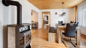 A modern interior with a wood-burning stove, a dining area with a bench, and a kitchen visible in the background. - Apartment 'Ferienwohnung Annette' with Shared Terrace and Wi-Fi (Gomadingen)