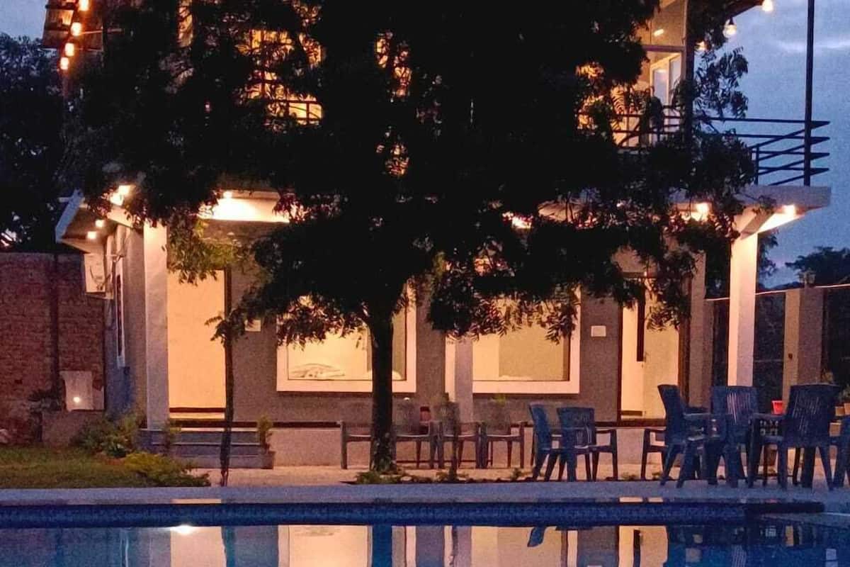 Un espace aménagé au bord de la piscine, où se reflètent les arbres et un bâtiment. Des chaises et des tables y sont disposées pour permettre de prendre les repas en plein air.