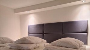 Un grand lit avec une tête de lit sombre, de nombreux oreillers et un plancher en bois.
