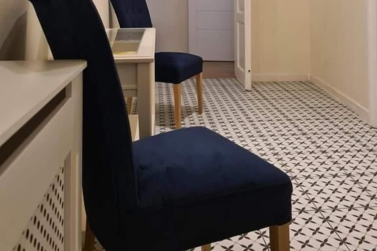 A hallway with a desk, two chairs, a painting on the wall, and a patterned floor.