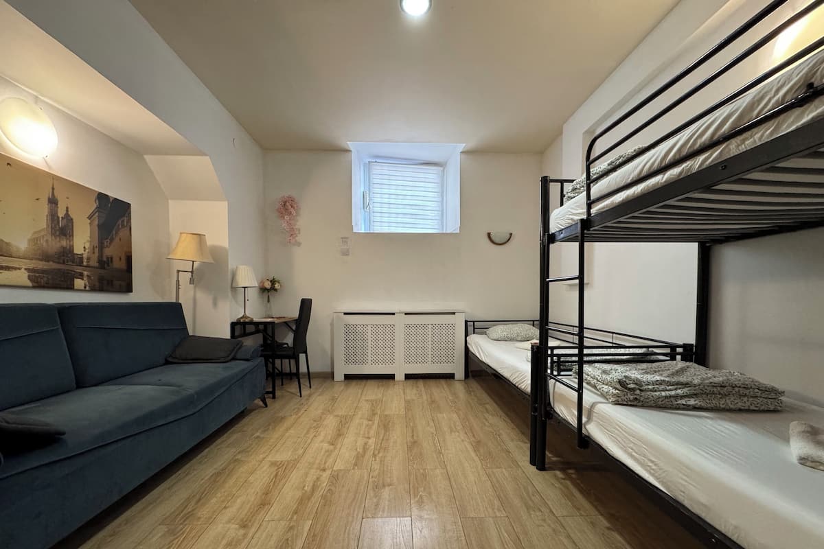 A compact room with a bunk bed, a sofa, a small table with a lamp, and a radiator.