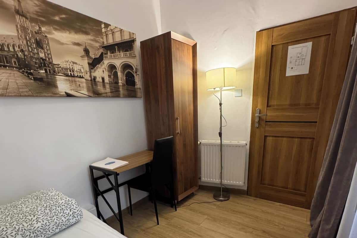 A hotel room with two beds, a desk, a chair, a lamp, and a wooden wardrobe.