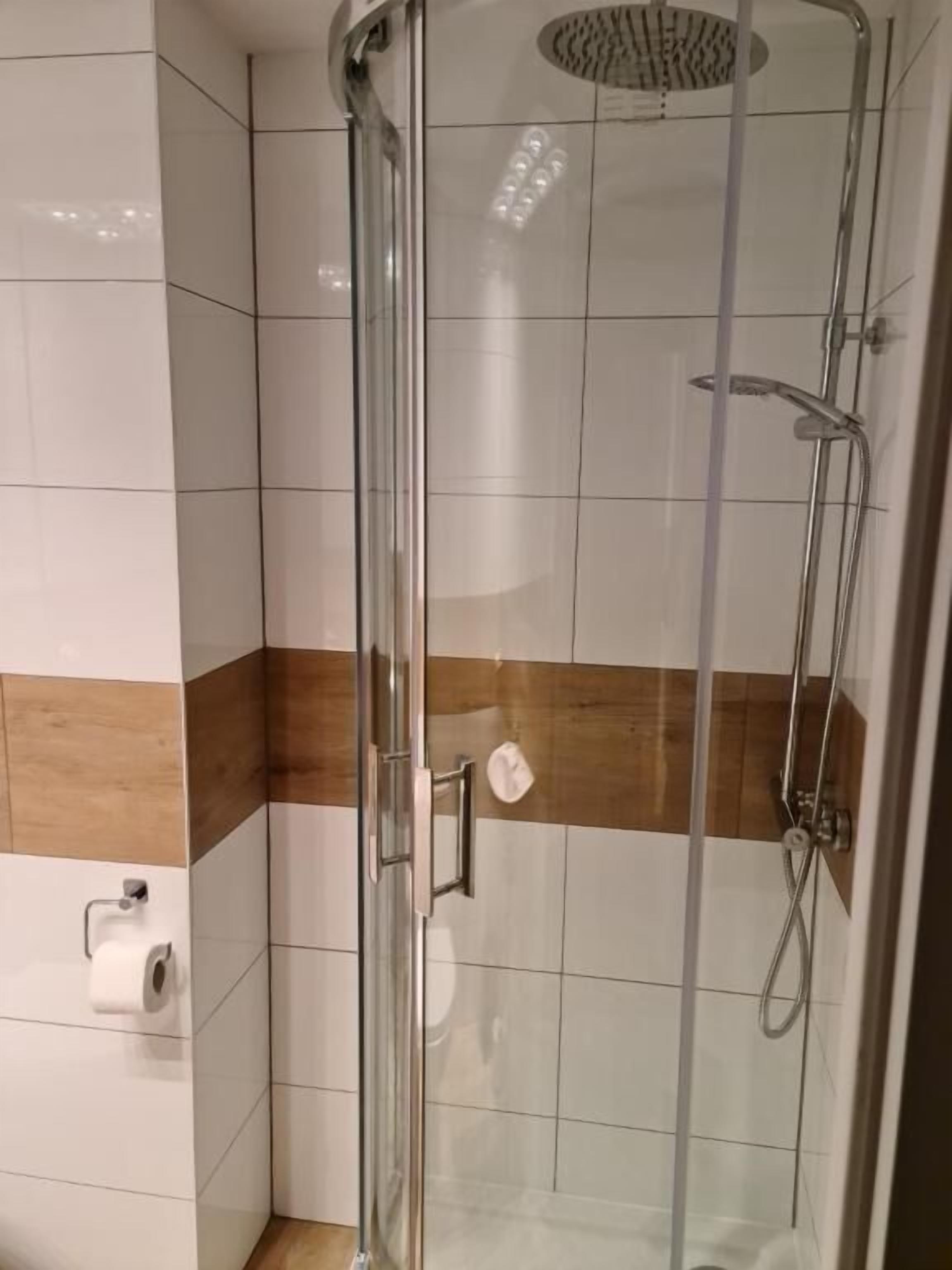 Une douche fermée par des parois en verre, dotée d’un pommeau de douche à main et d’un robinet mural.
