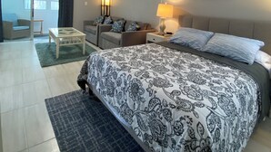 Ein Hotelzimmer mit einem großen Bett, einer Couch, einem kleinen Tisch und einer Lampe. Ein Fenster mit Vorhängen und ein Bild an der Wand sind ebenfalls zu sehen.