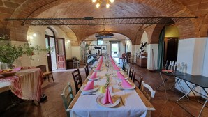Ein langer Esstisch ist für eine Mahlzeit in einem Zimmers mit Backsteinwänden, gewölbter Decke und einem Kronleuchter gedeckt.