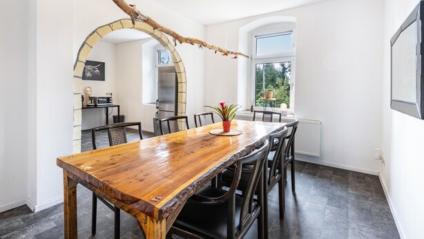 Un espace repas avec une table en bois, des chaises, un arrangement floral en guise de centre de table et une arche en briques.