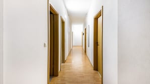 Un long couloir étroit, doté de planchers en bois et de murs blancs, qui mène à plusieurs portes.