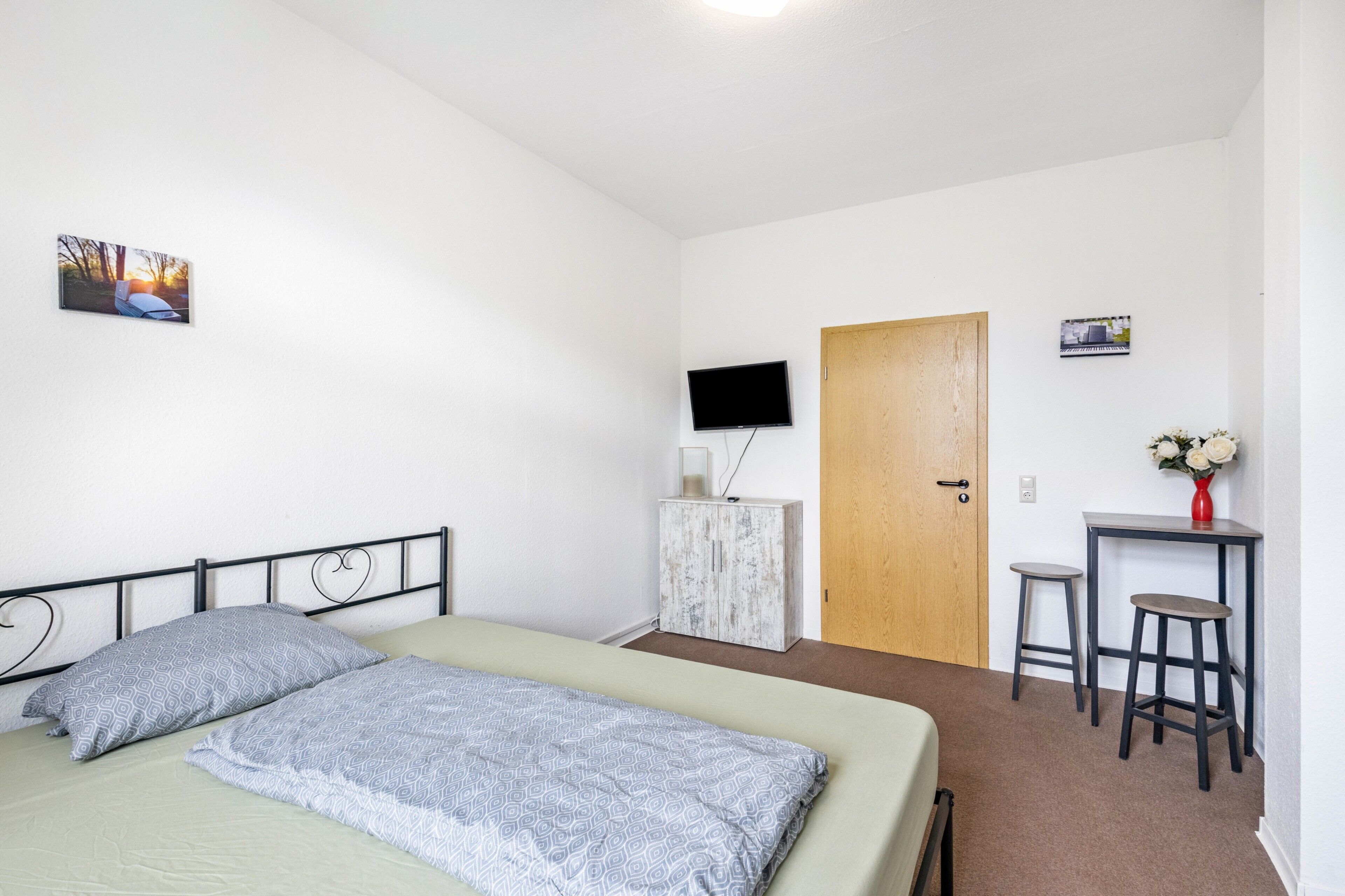 A bedroom with a bed, a television, a wooden door, and a small table with two stools.