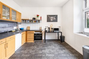 A kitchen with wooden cabinets, a dishwasher, a stove, a black countertop, a sink, a window, and a wall-mounted picture of a bull.