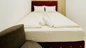 A small, single-bed room with a red headboard, a brown armchair, and a window with beige curtains. - Cozy Room Near FAC Platz | Shared Flat (Vienna)