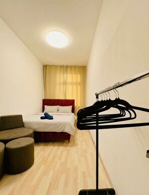A hotel room with a bed, a chair, a clothing rack, and a ceiling light.