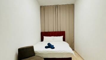 Ein kleines, schmales Hotelzimmer mit einem Einzelbett, einer runden Deckenleuchte und Holzboden.
