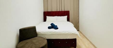 A small, narrow hotel room with a single bed, a round ceiling light, and a wooden floor.