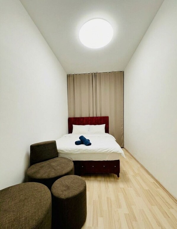 A small, narrow hotel room with a single bed, a round ceiling light, and a wooden floor.