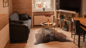 Una sala moderna con un sofá, una mesa de centro con flores, un televisor y una zona de comedor.