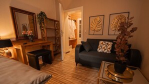 Una habitación acogedora con suelo de madera, un sofá con cojines estampados, un escritorio con lámpara y un espejo.