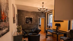 Een moderne woonkamer met een donker leren bank, een eethoek met een zwarte tafel, en een kroonluchter.
