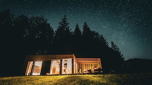 Een chalet met een groot open raam, houten buitenkant en uitzicht op de nachthemel.