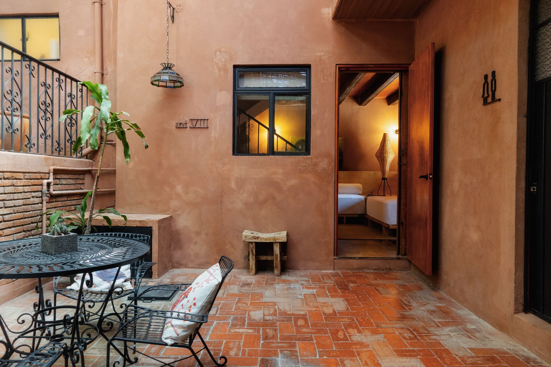A cozy courtyard with a tiled floor, a round metal table with chairs, a potted plant, and a small bench.