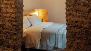 A bedroom with a brick wall archway, a bed with white bedding, and a nightstand with a lamp. - Casa Arrona Oaxaca (Oaxaca)